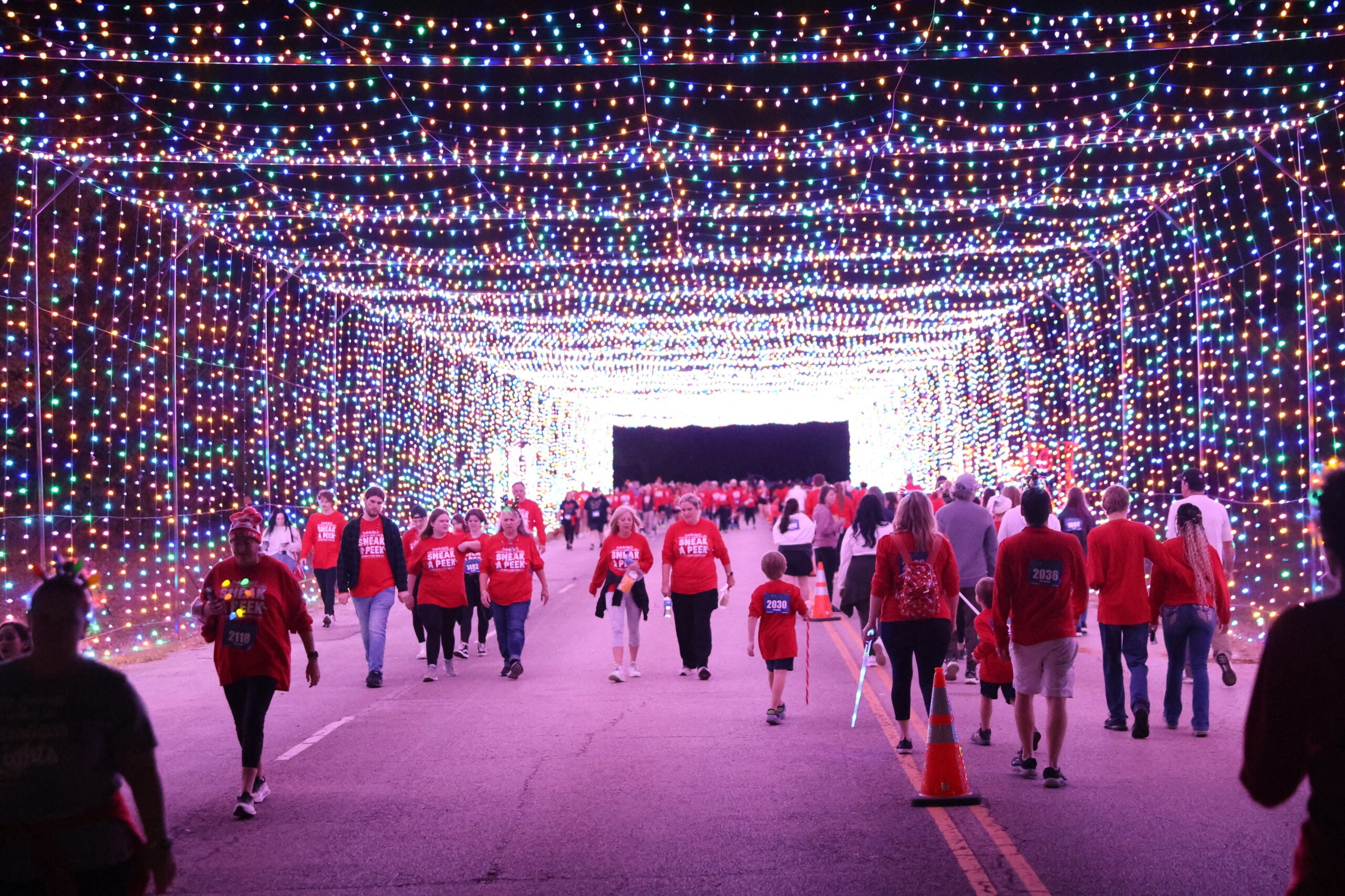 Walkers under an arched canopy of holiday lights